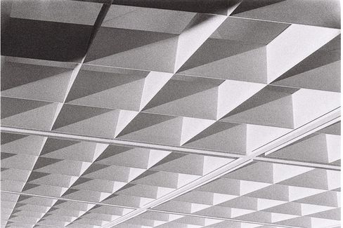 Schwarz-weiße Aufnahme einer Decke mit einem Muster aus dreidimensionalen, pyramidenförmigen Elementen in Reihen.