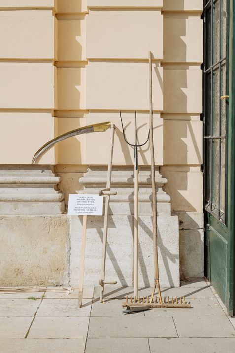 A scythe, pitchfork, and rake leaning against the MQ