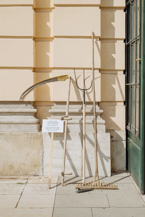 A scythe, pitchfork, and rake leaning against the MQ