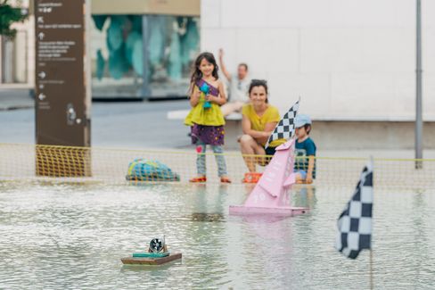 Children playing with small racing boats in the water basin at MuseumsQuartier Vienna during the Aquadrome summer activity.