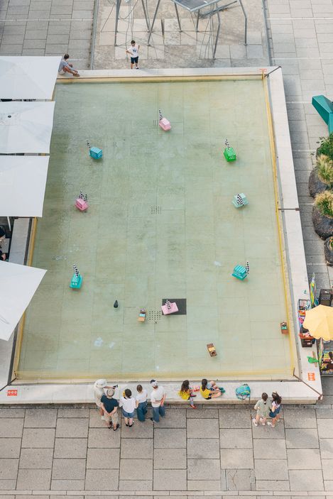 Aerial view of the Aquadrome water basin with multiple model boats in the courtyard of MuseumsQuartier Vienna.