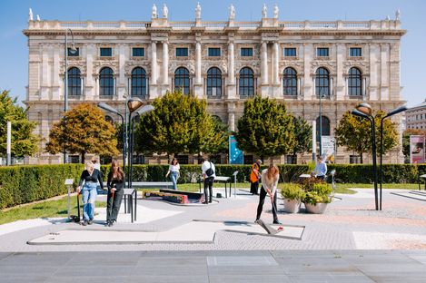 Multiple people play mini golf on a modern course in front of a historic building with a symmetrical facade.