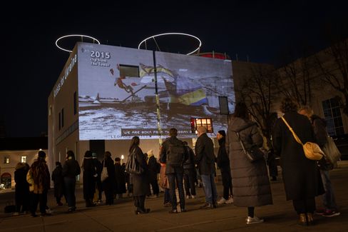 Menschen stehen nachts vor einem Gebäude, auf dessen Fassade ein Bild mit Text projiziert wird.
