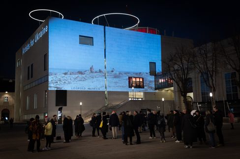 Menschen stehen abends vor dem Leopold Museum, auf dessen Fassade ein Bild mit der Aufschrift 'Artists for Ukraine' projiziert ist