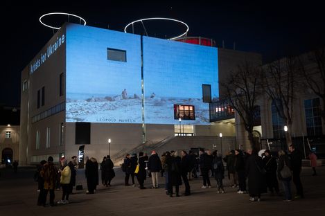Menschen stehen abends vor dem Leopold Museum, auf dessen Fassade ein Bild mit der Aufschrift 'Artists for Ukraine' projiziert ist
