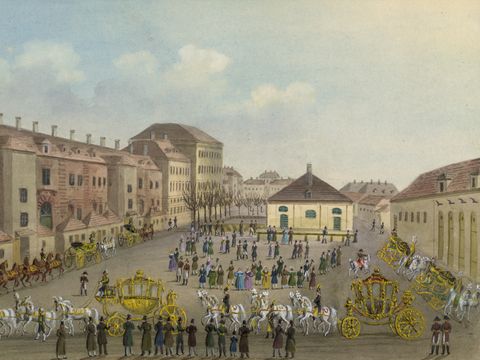 Historische Darstellung der Kaiserlichen Hofstallungen in Wien mit mehreren goldverzierten Kutschen und zahlreichen Menschen auf dem Hof