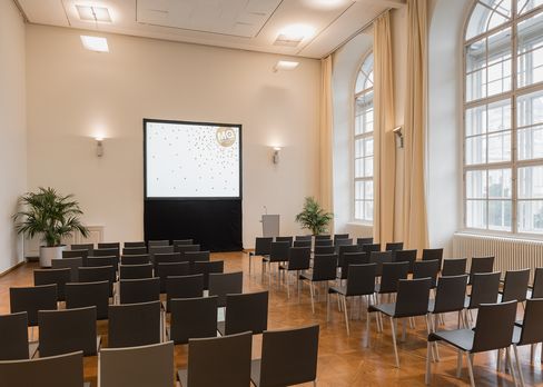 Conference room in the Baroque Suites at MuseumsQuartier Vienna with rows of chairs, a projection screen, and large windows.