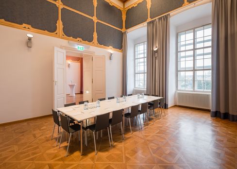 Large bright room with tall windows, parquet floor, decorative stucco ceiling, and a long table with chairs in the Baroque Suite at MuseumsQuartier Vienna