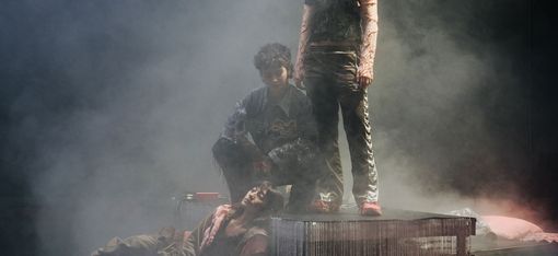 Drei Performer*innen stehen als Gruppe auf der Bühne – stehend, hockend und liegend