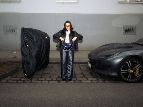 Person standing on a sidewalk between a bicycle covered with a black tarp and a parked sports car