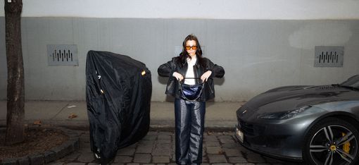 Person standing on a sidewalk between a bicycle covered with a black tarp and a parked sports car