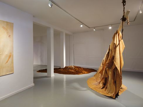 Installation with hanging ropes and piles of earth in a white gallery space.