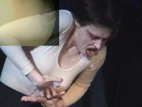 Woman with clenched teeth and tense facial expression holding her upper abdomen with both hands.