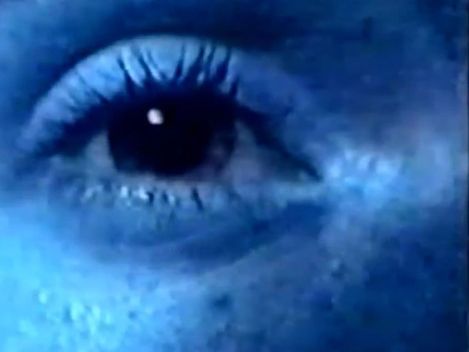 Close-up of a human eye with visible eyelashes and skin texture under bluish light.