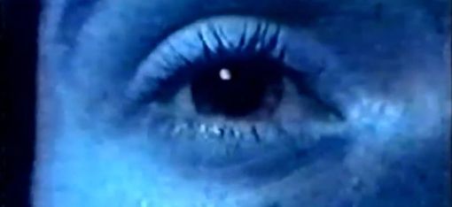 Close-up of a human eye with visible eyelashes and skin texture under bluish light.