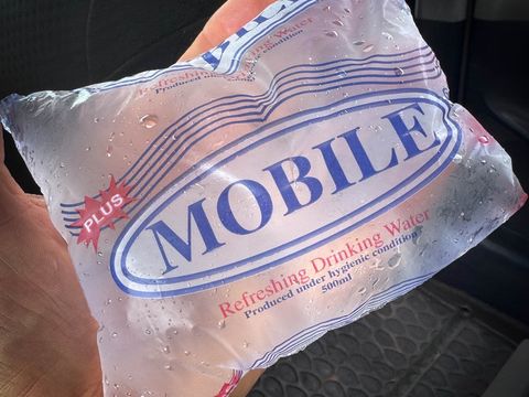 Hand hält eine durchsichtige, mit Wasser gefüllte Plastikverpackung mit der Aufschrift 'MOBILE' und 'Refreshing Drinking Water'