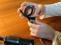 Hands holding a round black object with a handle over a wooden table.