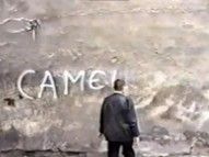 Man stands in front of a rough wall with the white text "CAMEL".