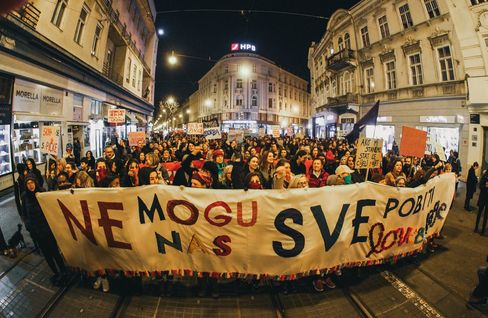 Large crowd at night on a busy street holding a large banner and multiple signs in a city with historic buildings.