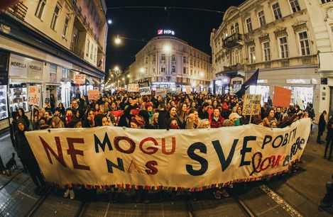 Large crowd at night on a busy street holding a large banner and multiple signs in a city with historic buildings.
