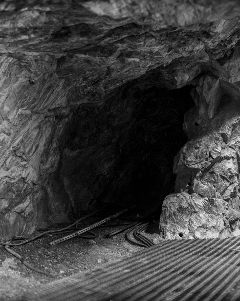 Entrance of a dark mine tunnel with rails and cables on the ground.