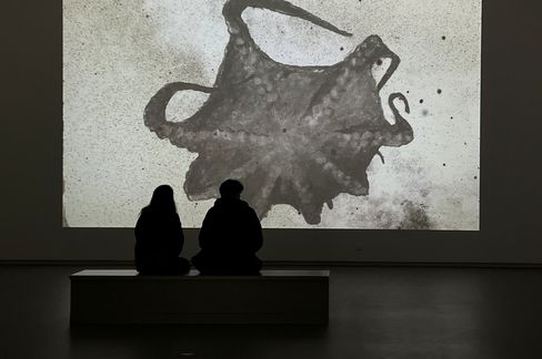 Woman with shoulder-length hair wearing a black buttoned shirt and glasses on her head standing in front of a brick wall.