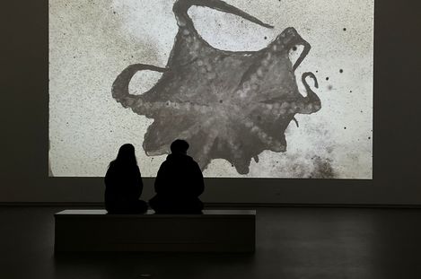 Woman with shoulder-length hair wearing a black buttoned shirt and glasses on her head standing in front of a brick wall.
