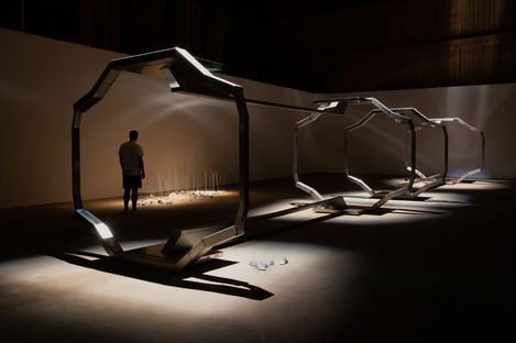 Person standing in front of a series of large octagonal metal frames in a dark room with light spots on the floor.