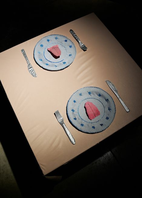 Table installation with embroidered plates, cutlery, and a textile object on a set table.