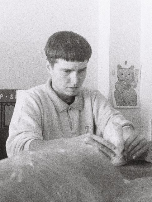 A person is sitting at a table holding something in their hands, with a wall displaying a picture of a waving cat visible in the background.