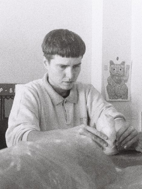 A person is sitting at a table holding something in their hands, with a wall displaying a picture of a waving cat visible in the background.