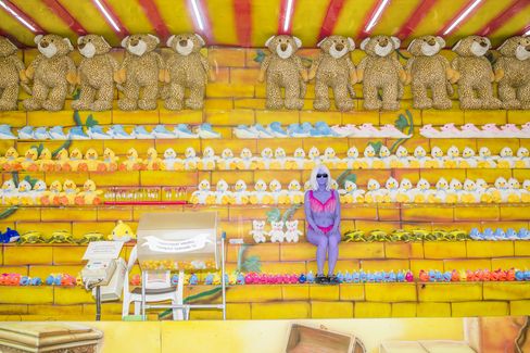 Female figure in purple clothing and sunglasses sitting on yellow steps with rows of plush bears, ducks, and other stuffed animals.