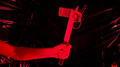 Red light illuminating an outstretched arm holding a homemade hammer wrapped with wire and tape.