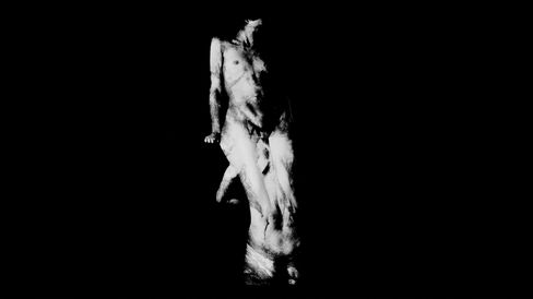 The image shows a high-contrast black-and-white depiction of a human figure against a deep black background, with the body only partially visible and appearing in a dynamic, slightly twisted pose. Due to the harsh lighting and blurring, the contours and details appear fragmented, creating an abstract, almost ghostlike effect.