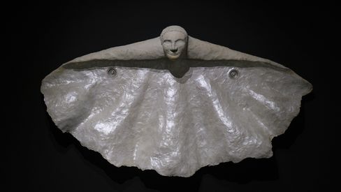 Sculpture of an abstracted butterfly with spread wings made of shiny material against a black background.