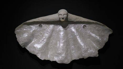 Sculpture of an abstracted butterfly with spread wings made of shiny material against a black background.