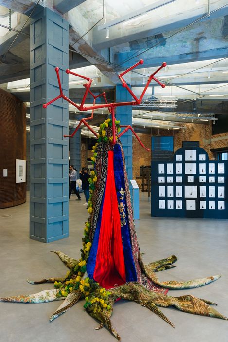 Large sculpture with red branching elements and a textile body in an exhibition hall.