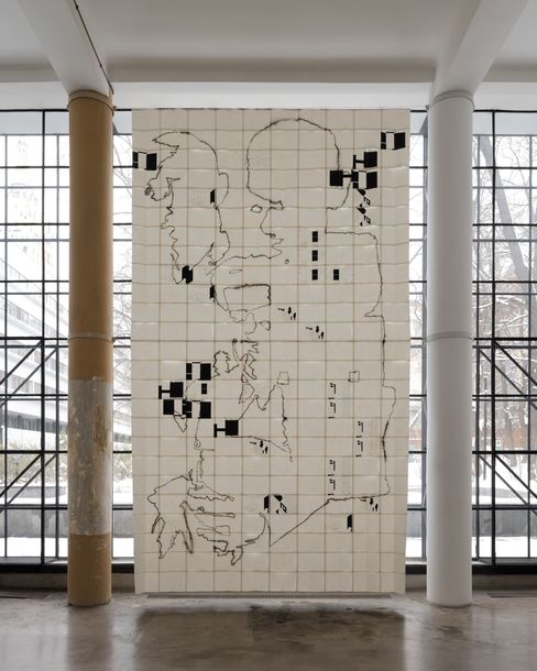 Großes Wandkunstwerk aus weißen Kacheln mit schwarzen Linien und schwarzen Quadraten in einem Raum mit großen Fenstern und zwei Säulen.