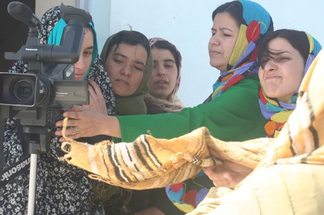 Several women operate a Panasonic video camera and hold a striped cloth.