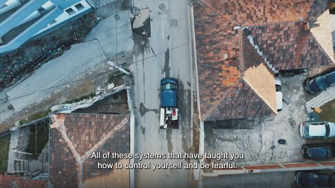 Aerial view of a residential area with red tiled roofs, a street, and several parked cars including a blue truck.