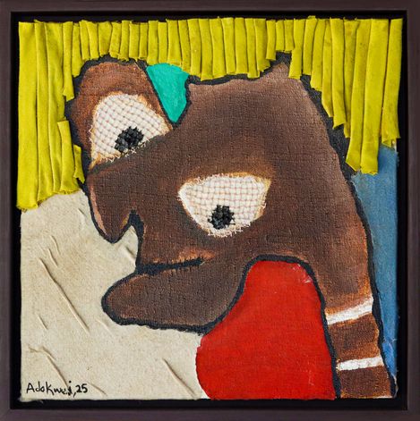 The image shows a framed abstract textile artwork depicting a stylized face.
The face is composed of various fabric pieces: brown areas form the head, white stitched eyes, yellow fabric strips as hair, a red shape in the lower area, and blue and beige background elements. The piece has an expressive, handmade, collage-like quality.