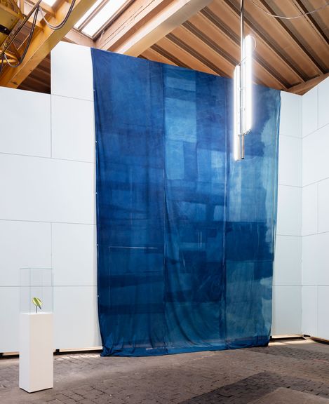 Large blue rectangular fabric hanging in a room with white walls and exposed wooden ceiling beams.