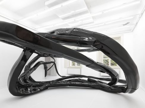 Black glossy sculpture with curved, intertwined organic shapes in a white room with windows.