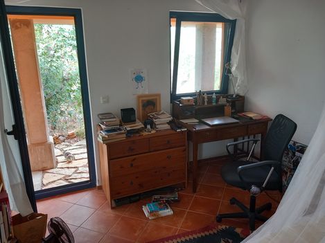 Small study room with desk, swivel chair, chest of drawers, books, and open window and door leading to garden.