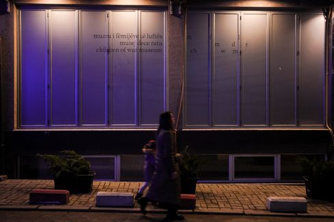 A woman and a child walk past a building at night with large closed windows and partially legible text.