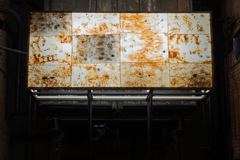 Rectangular white metal panels with rust stains arranged in a grid and mounted on a dark wall.
