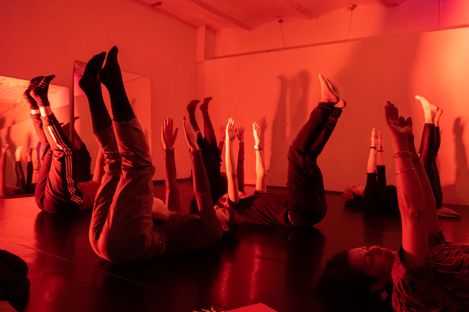 Several people lying on their backs with raised legs and arms in a room lit with red light.