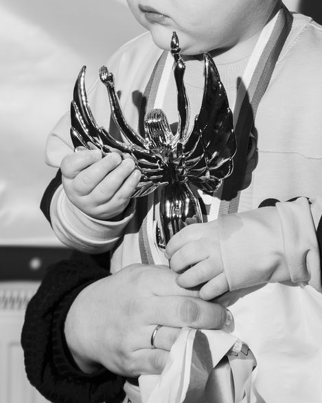 Child holding a shiny trophy shaped like a stylized bird with adult hands supporting it from below.