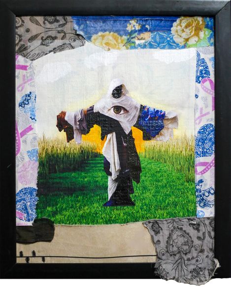 The image shows a framed mixed-media textile artwork featuring a central surreal figure. The figure stands on a green field, has outstretched arms, and an eye in the head area. Various fabrics, patterns, and collage elements form the background and border. The piece has a dreamlike, symbolic quality.