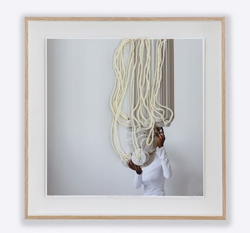 Person in white top holding two round, pleated objects under hanging long white ropes.